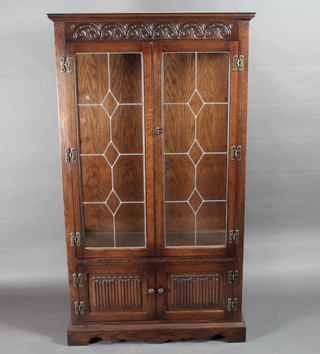 A carved oak display cabinet, the shelved interior enclosed by lead glazed doors, the base enclosed by linenfold panelled doors  34"w x 13"d x 62"h