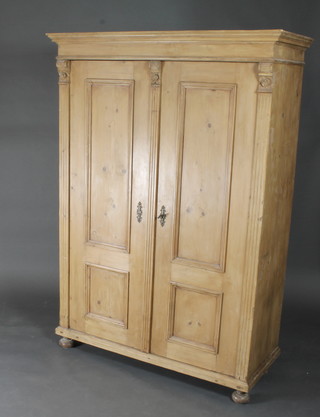 A Continental pine fitted wardrobe with moulded cornice enclosed by panelled doors, raised on bun feet 50"w x 22"d x 72"h