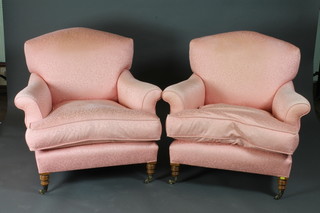 A pair of armchairs upholstered in pink material raised on turned  supports ending in brass caps and castors