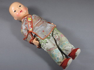 An Oriental doll wearing a silk jacket and 2 silk handkerchiefs