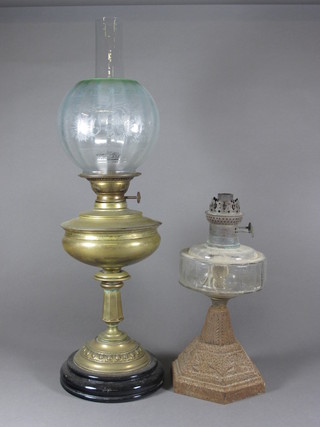 A brass oil lamp reservoir with clear glass chimney and shade and 1 other with clear glass reservoir and iron base