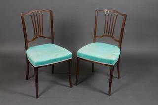 A pair of Edwardian oak stick and rail back bedroom chairs with upholstered seats raised on outswept supports