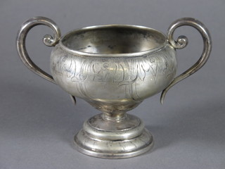 An engraved white metal twin handled bowl raised on a circular  spreading foot
