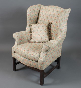 A George III style wing armchair, having foliate tapestry woven upholstery raised on square chamfered legs united by stretchers