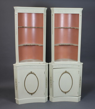 A pair of cream painted concave standing corner cabinets in the  neo classical taste, with dentil moulded cornices above 2 shaped  shelves with cupboard door below, raised on plinth bases 71"h x  26"w x 14"d