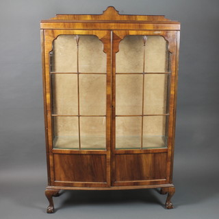 A 1930's walnut bow front display cabinet, having a pair of bar glazed doors enclosing glass shelves, raised on squat cabriole  legs, claw and ball feet 66"h x 41"w x 14"d
