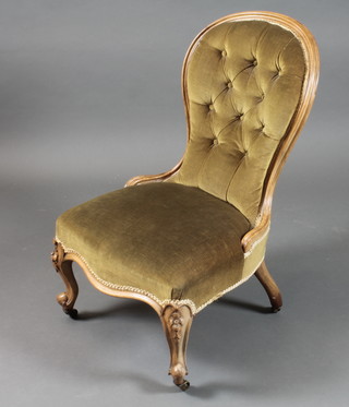 A Victorian walnut low seat nursing chair, having dark green buttoned dralon upholstery, raised on floral carved cabriole legs,  scroll feet and casters
