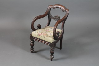 An early Victorian walnut childs elbow chair with scroll carved cresting rail and spar above a woolwork Trafalgar seat, raised on  baluster turned legs