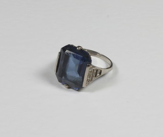 A lady's white metal dress ring set a rectangular cut blue synthetic spinel, flanked by brilliant shoulders