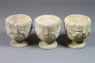 A set of 3 reconstituted stone garden urns, the rims decorated  with a Greek key pattern above bunches of grapes, raised on  circular spreading bases 11"diam x 9.5"h