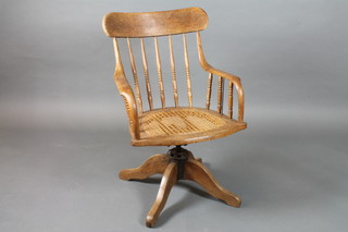 A late 19th Century oak swivel desk chair with cane seat on quadripartite base