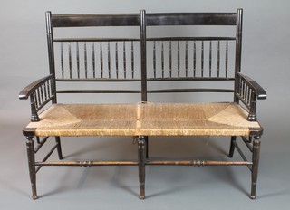 In the manner of William Morris, an ebonised "Sussex" style  double chair back settee with turned spindles, scroll arms and rush seats, raised on ring turned tapered legs, late 19th  Century 47"w  ILLUSTRATED