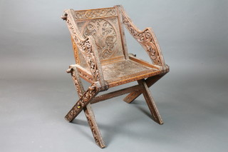 An Edwardian carved oak Glastonbury chair, the frame and arms  relief carved with vines, the back centre with floral cartouche and  the seat carved with dolphins, dated 1907
