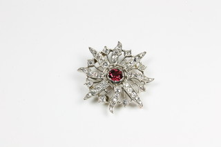 A gold brooch in the form of a star set garnet to the centre, surrounded by diamonds, approx 1.2ct