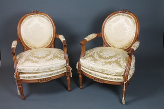 A pair of Louis XV style stained beechwood fauteuils, having floral cut satin upholstery, raised on turned tapered, fluted legs