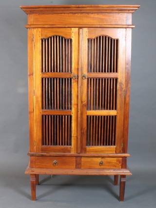 A hardwood cabinet enclosed by lattice panelled doors above 2 drawers with brass drop handles, raised on square tapered  supports