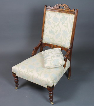 A late Victorian mahogany low seat salon chair having floral tapestry woven upholstery raised on turned legs and casters
