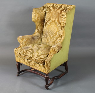 A Queen Anne style walnut framed wing arm chair with floral  cut velvet upholstery, raised on baluster turned legs united by  shaped stretcher, with casters