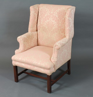 A George III style wing open arm chair having pink and cream  floral woven upholstery, raised on square legs united by an H  stretcher