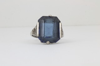 A lady's white metal dress ring set a rectangular cut blue synthetic spinel, flanked by brilliant shoulders