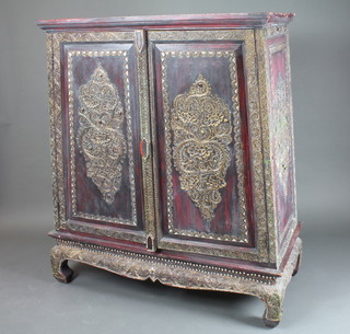 An unusual Indian hard wood side cabinet, parcel gilded and decorated with Arabesques, the 2 fielded panelled cupboard doors  enclosing 2 shelves, raised on a shaped plinth base 56"h x 44"w  x 24"d