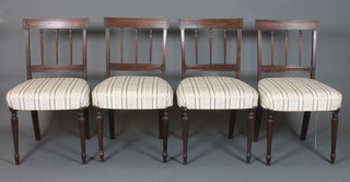 A set of 4 Regency style mahogany dining chairs with tablet cresting rails and spindle backs, stuff-over seats on tapered and  turned legs