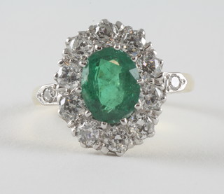 An 18ct yellow gold dress ring set an oval cut emerald  surrounded by diamonds, approx 1.80/1.30ct