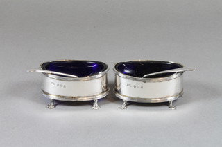 A pair of oval silver salts raised on panel supports, Birmingham 1920 by Walker & Hall complete with blue glass liners and  condiment spoons, 2 ozs