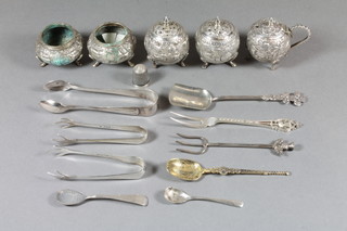 An Eastern 5 piece embossed white metal condiment set comprising pair of peppers, pair of salts and a mustard pot, 3  pairs of silver sugar tongs, a silver thimble, 2 silver mustard  spoons, a silver pickle fork and a silver gilt model of the  anointing spoons, 2 ozs,