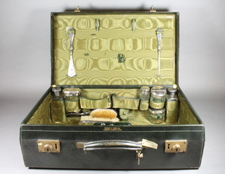 A Mappin & Webb green leather vanity case containing 6 glass bottles with silver lids, a silver handled shoe horn, do. button  hook, 2 manicure implements, a scent bottle corkscrew and a  silver backed hand mirror and hairbrush, mostly London 1917