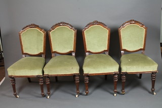 A set of 4 late 19th Century oak dining chairs, the shaped cresting rails carved with bell flowers above a padded back and  stuff-over seat, raised on fluted turned tapered legs and casters