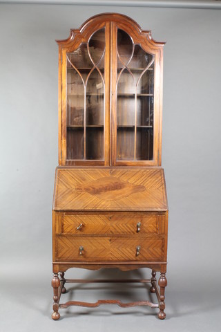 A 1930's Queen Anne style mahogany bureau with arch shaped  top fitted adjustable shelves enclosed by astragal glazed panelled  doors, the fall enclosing a fitted interior above 2 long drawers,  with wavy framed stretcher on bun feet 83"h x 30"w x 18"d