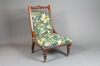 An Edwardian carved walnut easy chair upholstered in William Morris material raised on turned supports
