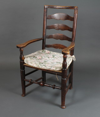 An 18th Century oak ladder back elbow chair having shaped  arms, rush seat, raised on turned legs with pad feet