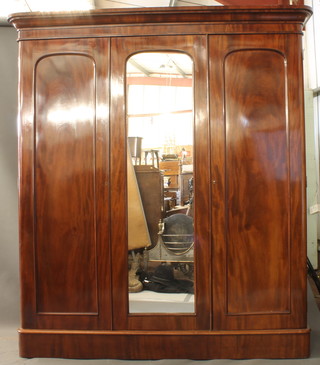 A good mid Victorian mahogany triple wardrobe having a plain  moulded cornice above a central mirrored door flanked by a pair  of fielded panelled cupboard doors enclosing an arrangement of 4  drawers raised on plinth base, 84"h x 77"w x 24"d