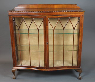 A 1920's mahogany serpentine display cabinet, having gadrooned  top above a pair of bar glazed doors enclosing 2 glass shelves,  raised on squat cabriole legs, claw and ball feet 50"h x 48"w x  14.5"d