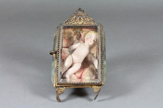 A miniature porcelain doll of a baby, arms f, 4" contained in a  gilt metal and faceted glass cabinet 5"