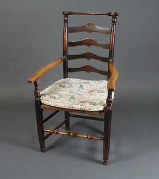 An 18th Century oak ladder back elbow chair having shaped arms above a rush seat, raised on tapered legs