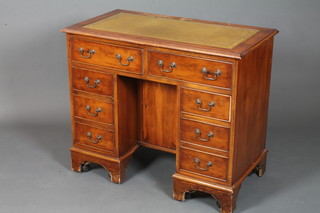A George III style yew wood kneehole desk, the top inset green  leather gilt tooled skiver, above an arrangement of 8 drawers  flanking a cupboard door, raised on shaped plinth base 31"h x  36"w x 20"d