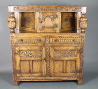A 17th Century style oak court cupboard having foliate relief  carved frieze above a cupboard door flanked by cup and cover  supports with a further 2 drawers and 2 cupboard doors below,  raised on guilloche carved end stiles, 56"h x 52"w x 18"d