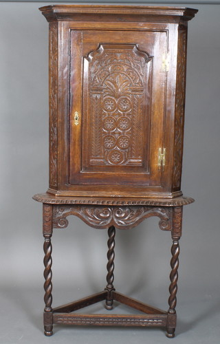 An 18th Century style carved oak corner cupboard on stand, having a foliate carved panelled cupboard door enclosing 3  shaped shelves, raised on barley twist supports united by  stretchers 67"h x 31"w x 17"d