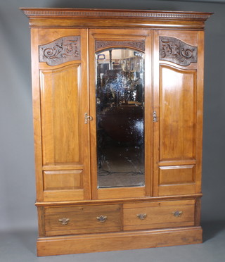 A late Victorian walnut triple wardrobe having dentil moulded  cornice above a mirror plate flanked by 2 foliate relief carved  panelled cupboard doors with 2 drawers below, raised on plinth  base 83"h x 65"w x 23"d