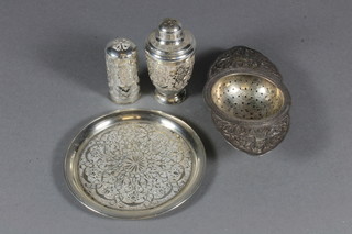 An Eastern embossed white metal tea strainer, do. tray and 2 pepperettes