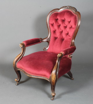 A mid Victorian walnut framed low seat armchair, having foliate and bell flower carved frame and maroon buttoned velvet  upholstery, raised on cabriole legs scroll feet