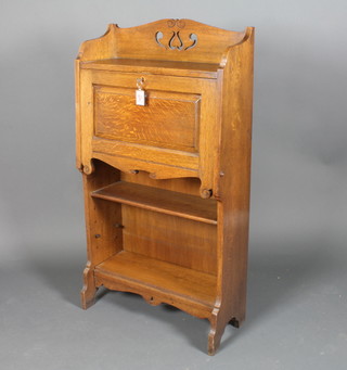 An Arts & Crafts light oak students bureau, the upper section  with pierced three-quarter gallery, the fall front enclosing a fitted  interior with pigeon holes above a bookcase 50"h x 27"w x 10"d
