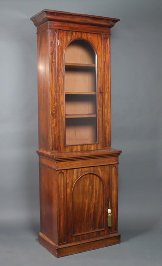 A Victorian mahogany bookcase on cabinet the upper section with moulded cornice, fitted shelves enclosed by an arched panelled door, the fitted a cupboard, raised on a platform base 83"h x 30"w x 30"d 