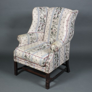 A Georgian style winged armchair upholstered in floral material, raised on square supports