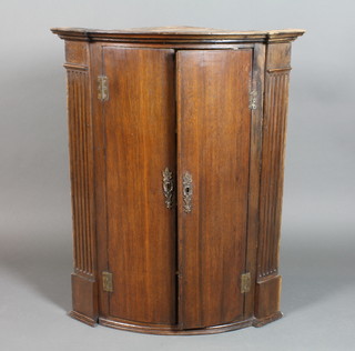 A Georgian oak bow front corner cabinet with moulded cornice and fluted columns to the sides, fitted adjustable shelves enclosed by panelled doors 38"h x 30"w x 20 1/2"d