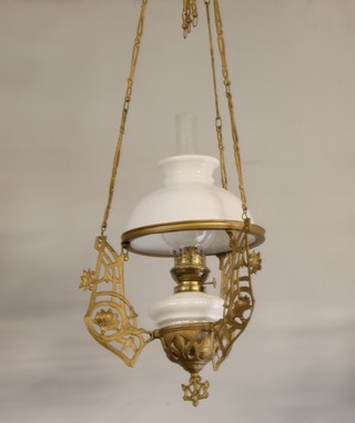 An Art Nouveau opaque glass hanging oil lamp contained in a pierced gilt metal frame