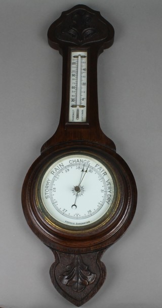 An aneroid barometer and thermometer with enamelled dial contained in a carved oak wheel case 